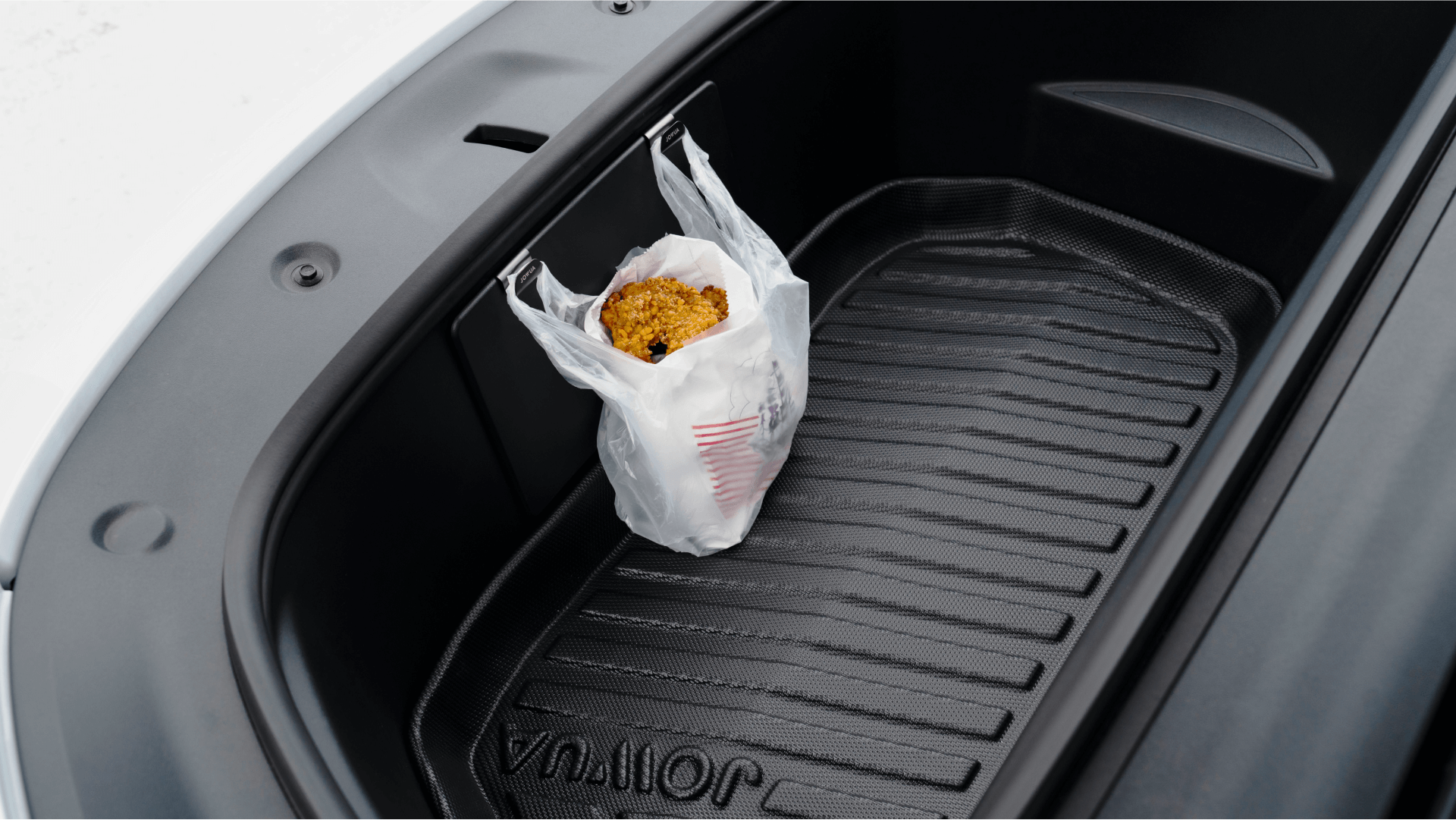 A plastic bag holding food items, including a container of popcorn, is neatly hung on the JOWUA Front Trunk Hook in the front trunk storage of a Model Y. The open trunk reveals its clean, lined interior.