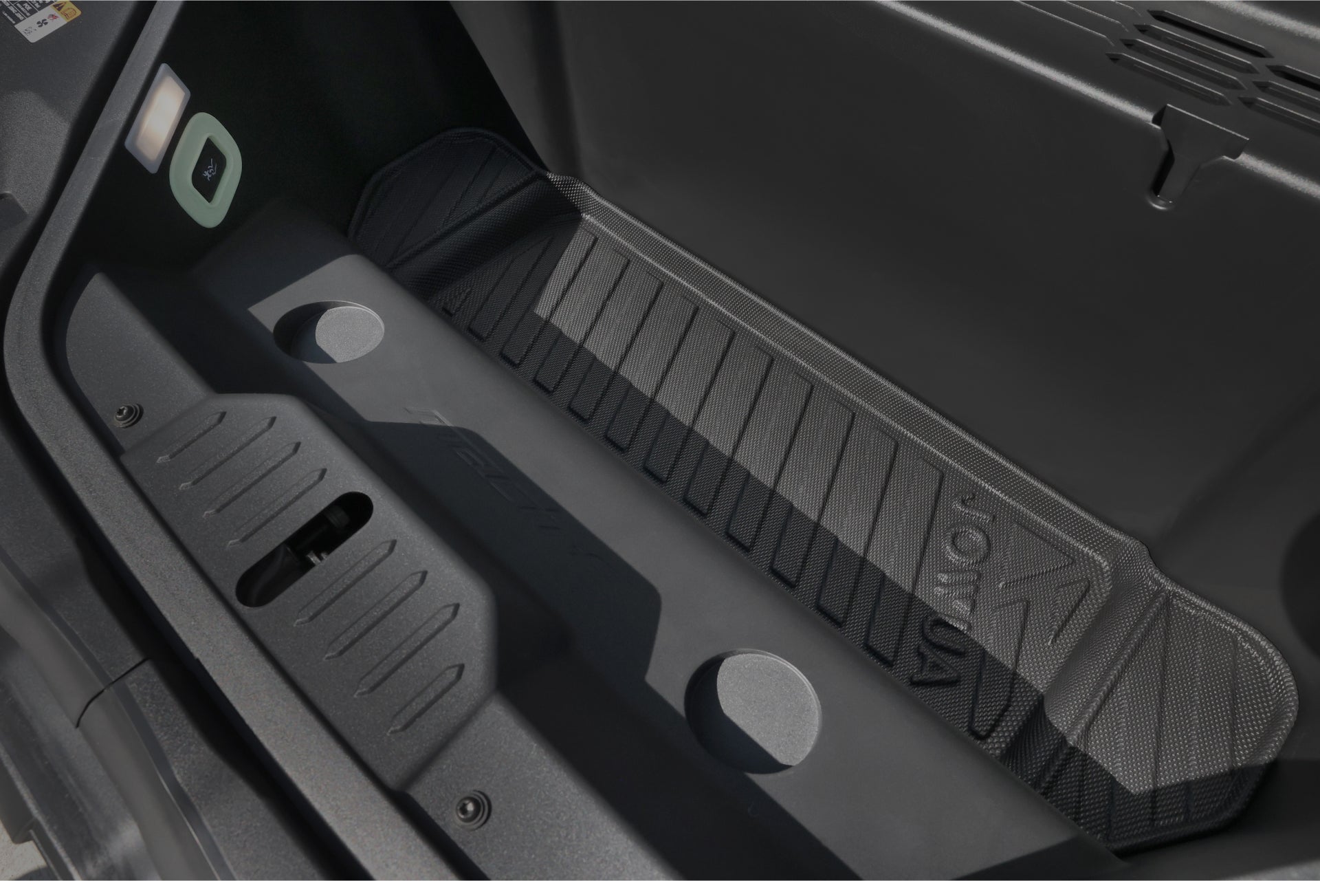 The image showcases the storage compartment of a vehicle, featuring JOWUA's All Weather Trunk Liners specifically designed for the Ford Mustang Mach-E. The liner boasts a textured floor and includes grooves and circular indentations to secure items effectively. Its foldable design complements the predominantly black color scheme.