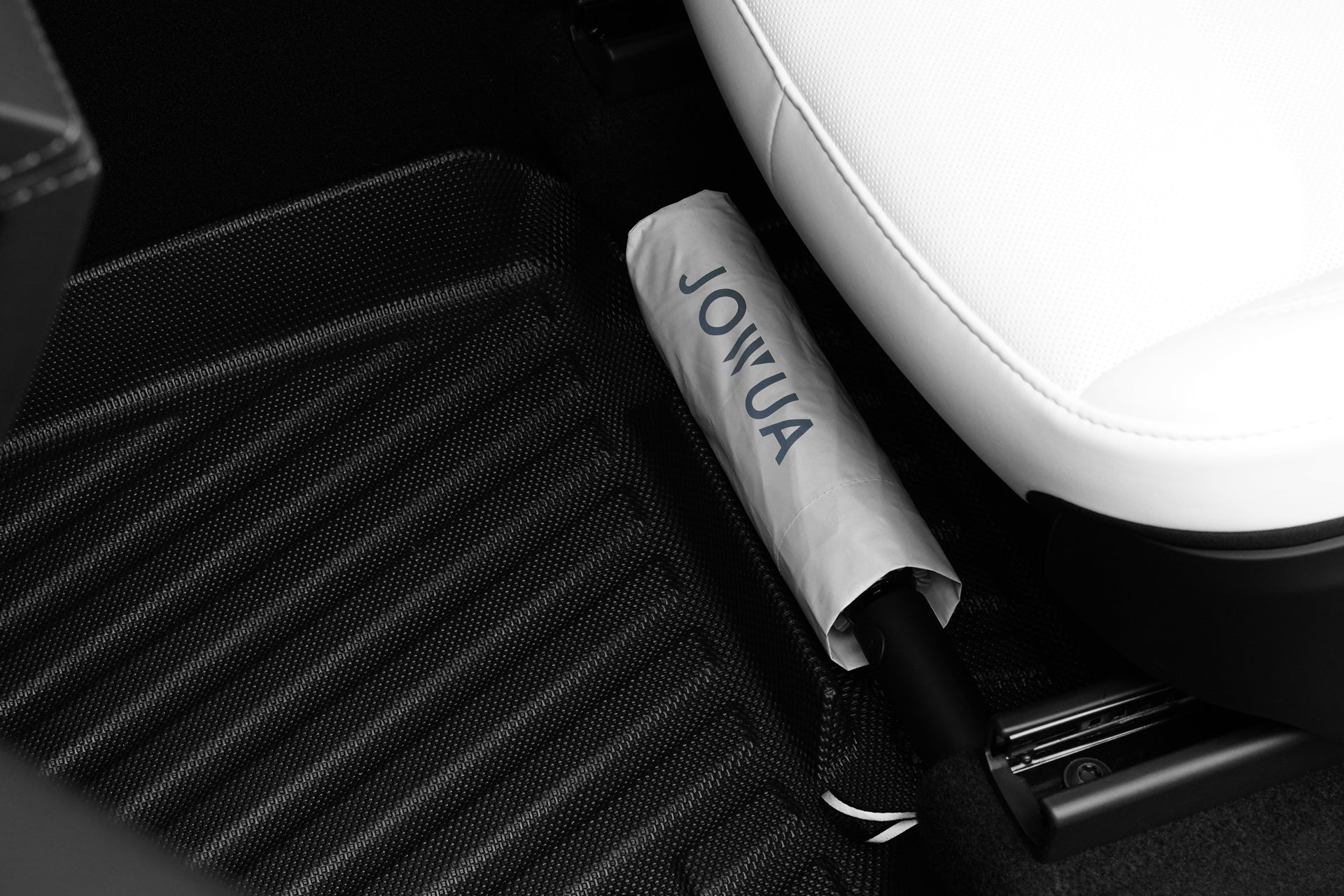 A folded umbrella with a white cover labeled "JOWUA" sits on the floor next to a white car seat and sleek Model Y 2025+ Interior / Trunk Full Coverage Liner Combo, the perfect all-weather accessory by JOWUA.