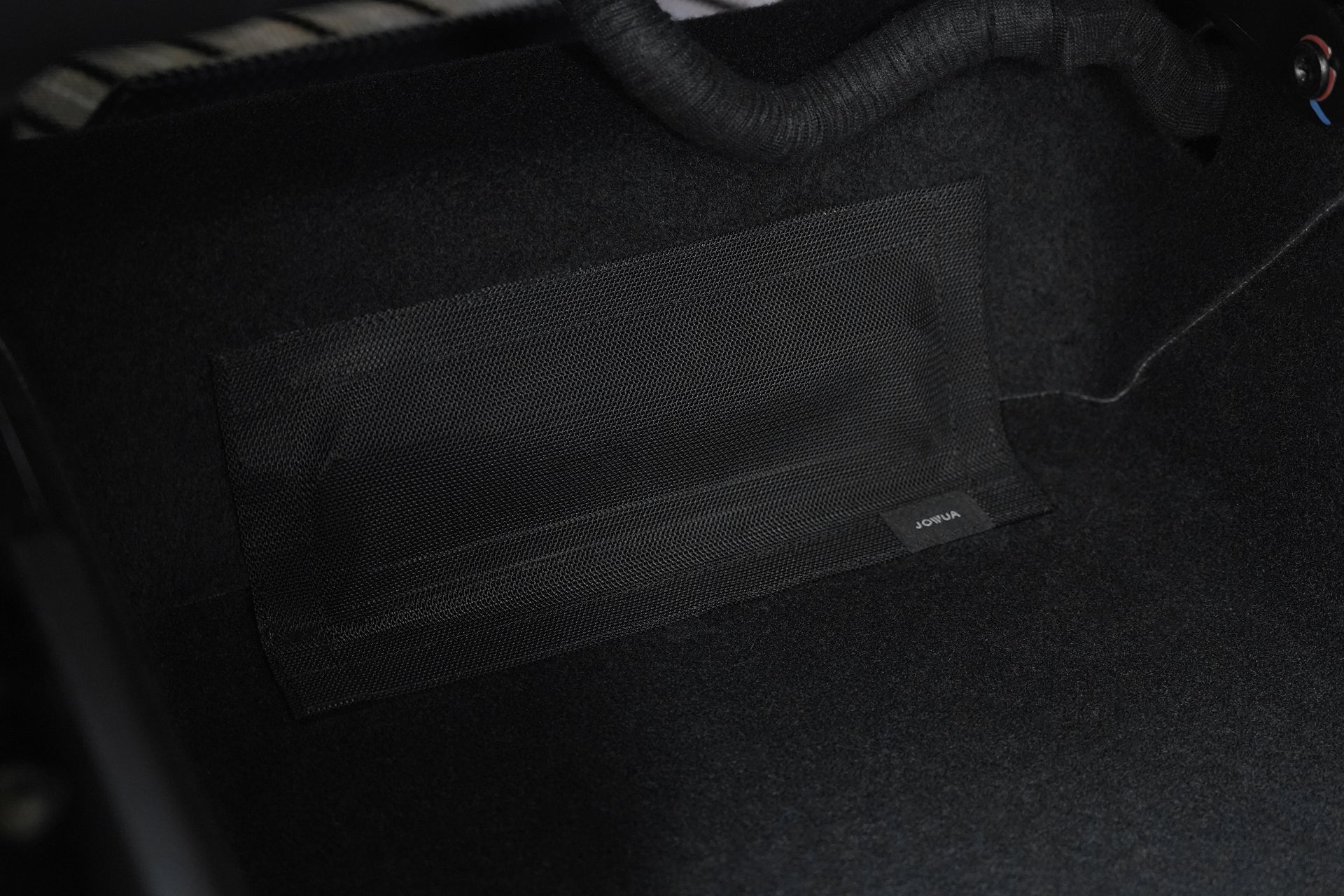 Close-up of a black mesh pocket on the carpeted floor of a vehicle, ideal to pair with the JOWUA Model Y 2025+ Interior / Trunk Full Coverage Liner Combo for enhanced organization and style.