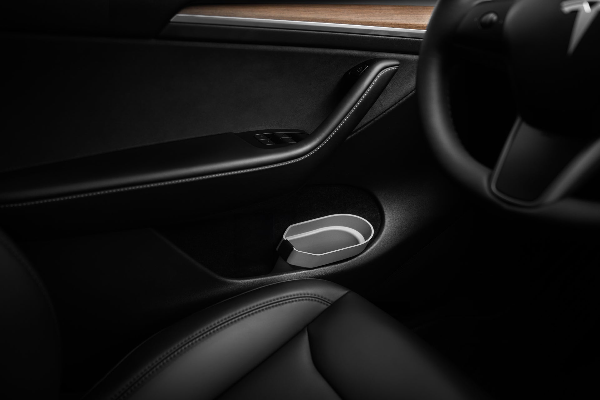 Close-up of a Tesla Model S interior featuring a black leather seat, a sleek door panel enhanced with a wood accent, and integrated with the Door Side Storage Box set by JOWUA, adding convenience. A cup holder is also visible, while the steering wheel appears partially on the right side of the image.