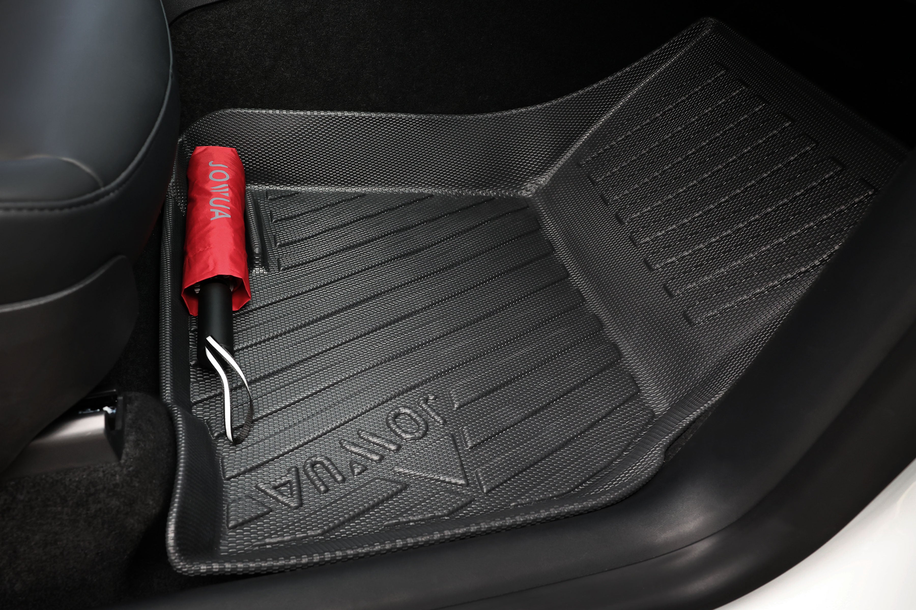 The JOWUA All Model Y All-Weather Floor Liners Combo (Juniper 2025+ / 2021-2024) feature grooves for optimal grip. A red umbrella with a black handle, also labeled "JOWUA," rests on the mat, while the car seat and door frame edges show off sleek design and protection for your Model Y interior.