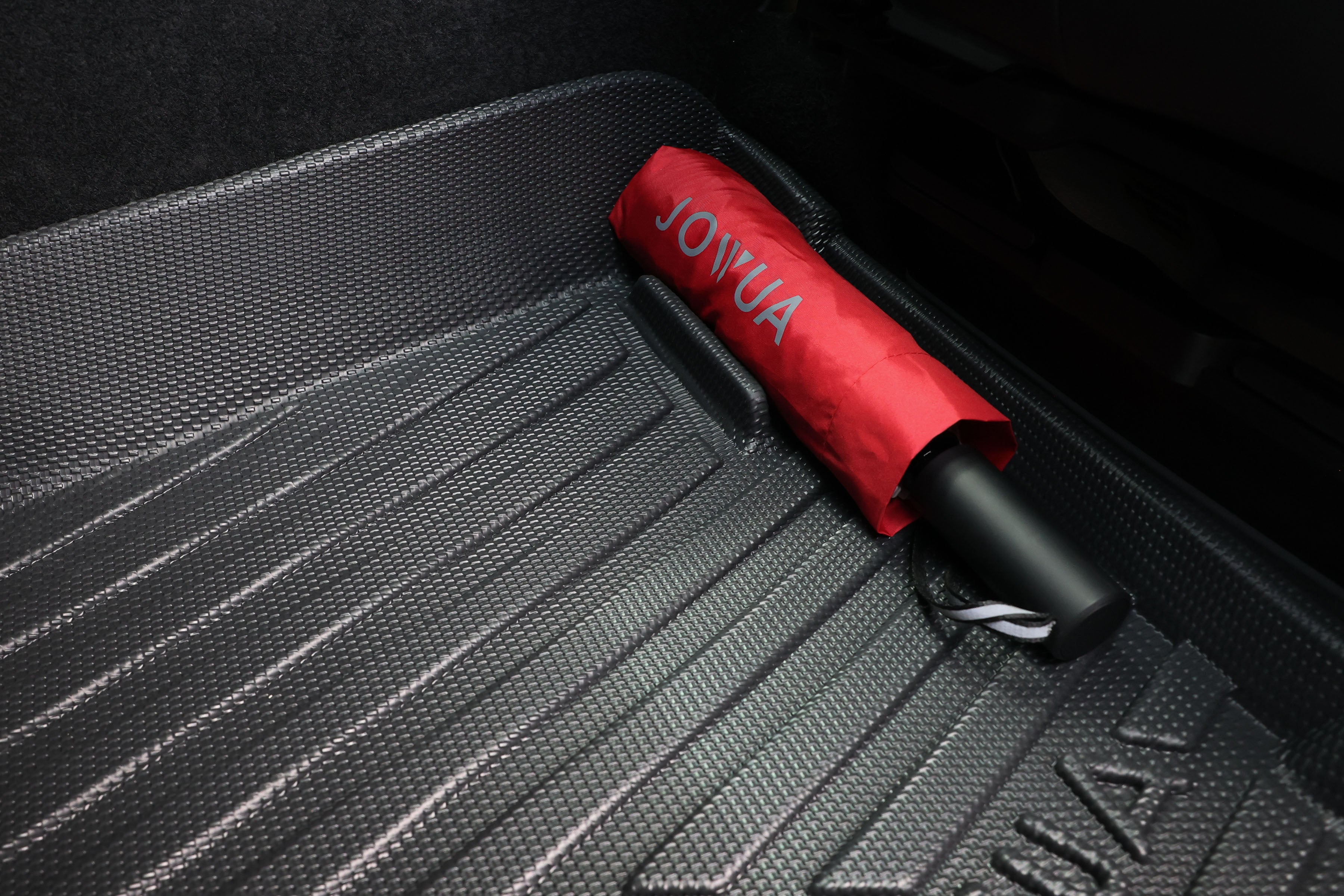 A red JOWUA umbrella with a black handle rests on All Model Y All-Weather Floor Liners Combo, ideal for Tesla Model Y (Juniper 2025+ / 2021-2024), highlighting essential accessories for your journey.