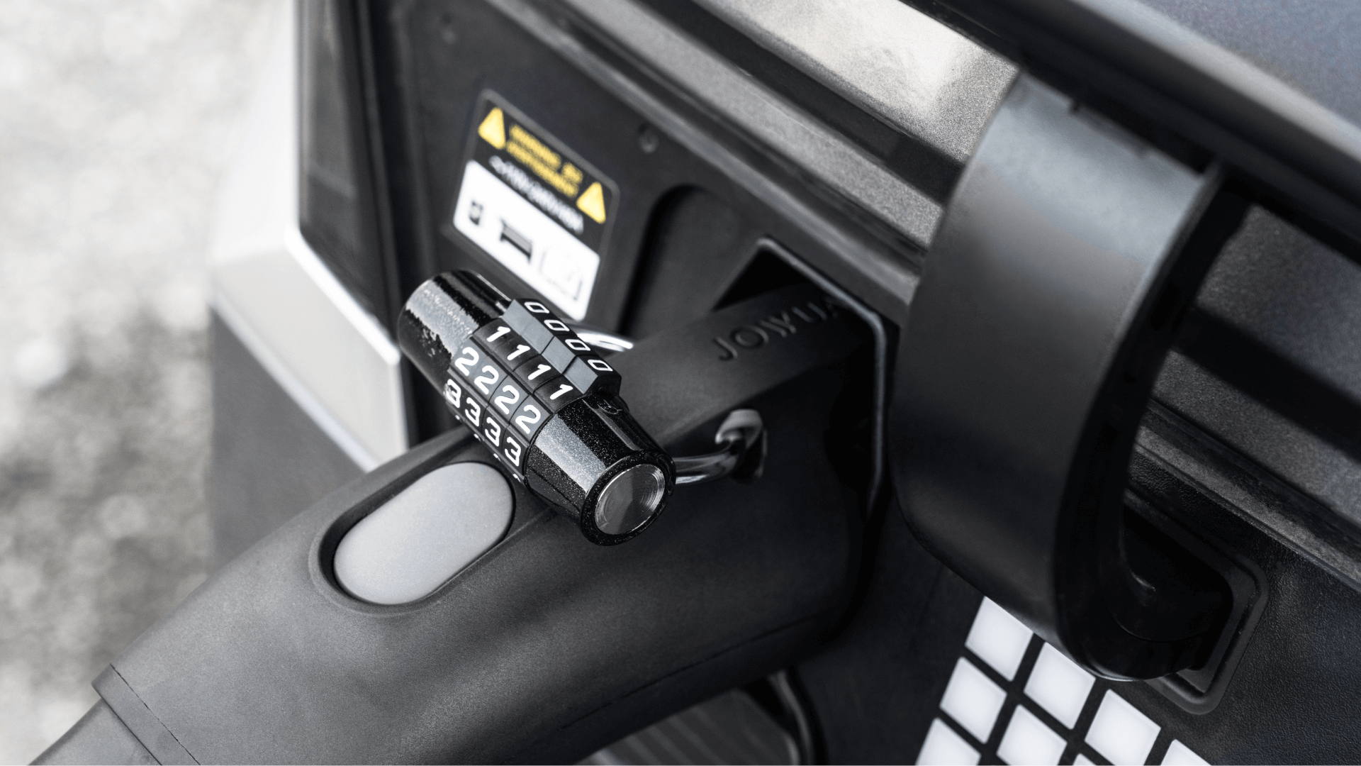 Close-up of a JOWUA TPC(NACS) to J1772 Adapter securing a handle on a piece of equipment, highlighting connector durability. The adapter displays numbers, set against a grayscale industrial environment.