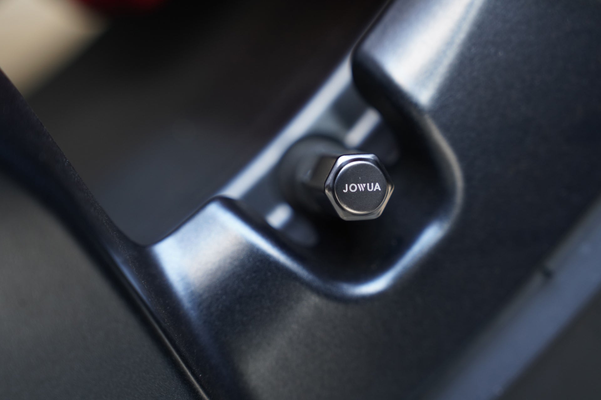 Close-up of a black hexagonal bolt engraved with "JOWUA," partially encircled by matte black metal—an essential detail in the JOWUA Portable Air Compressor + Charging Solution Kit.