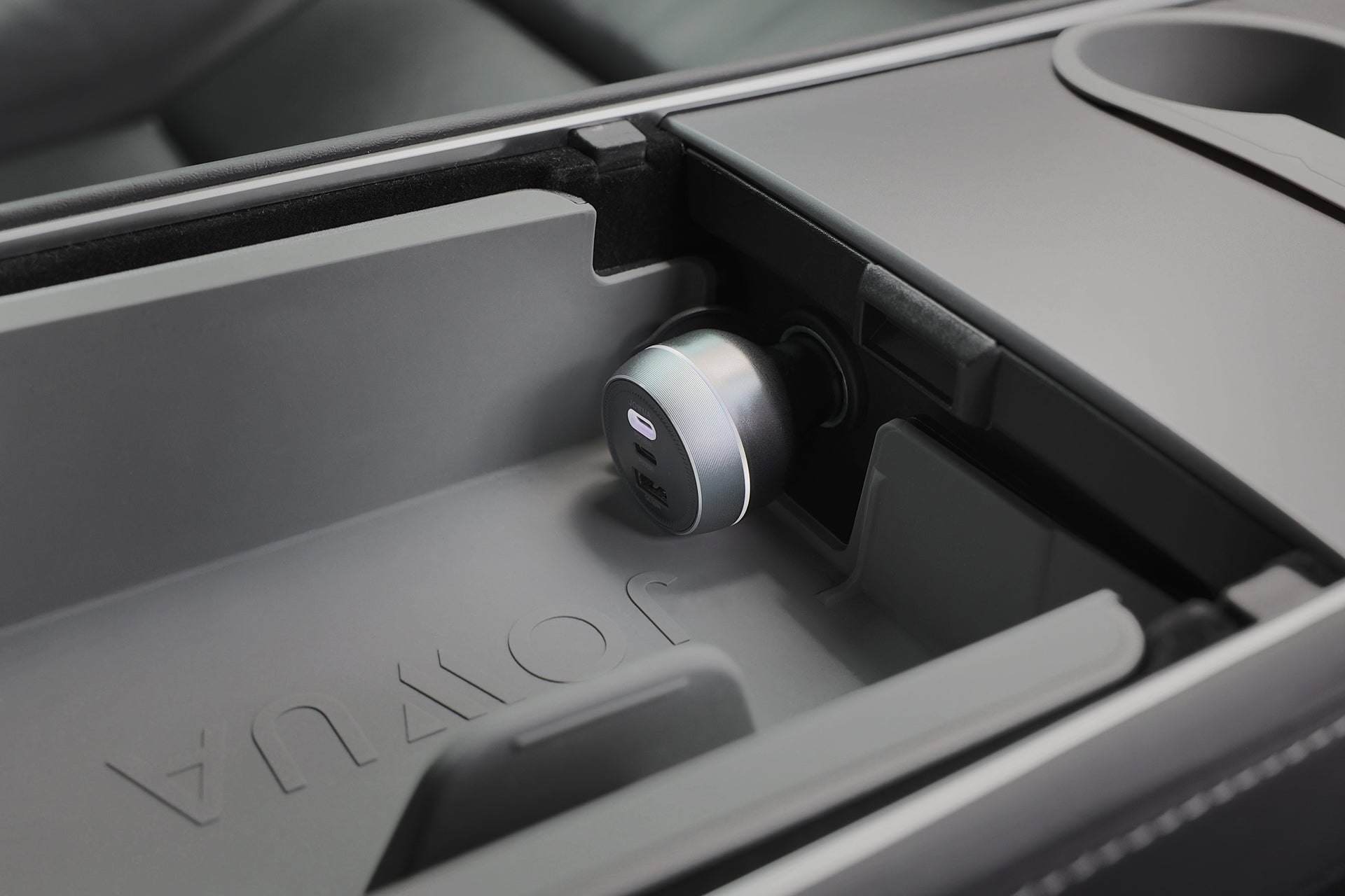 JOWUA Portable Air Compressor + Charging Solution Kit sits in the car console, plugged into a USB port amid smooth gray surfaces with "JOWUA" embossed—ideal for keeping Tesla tires inflated on the go.