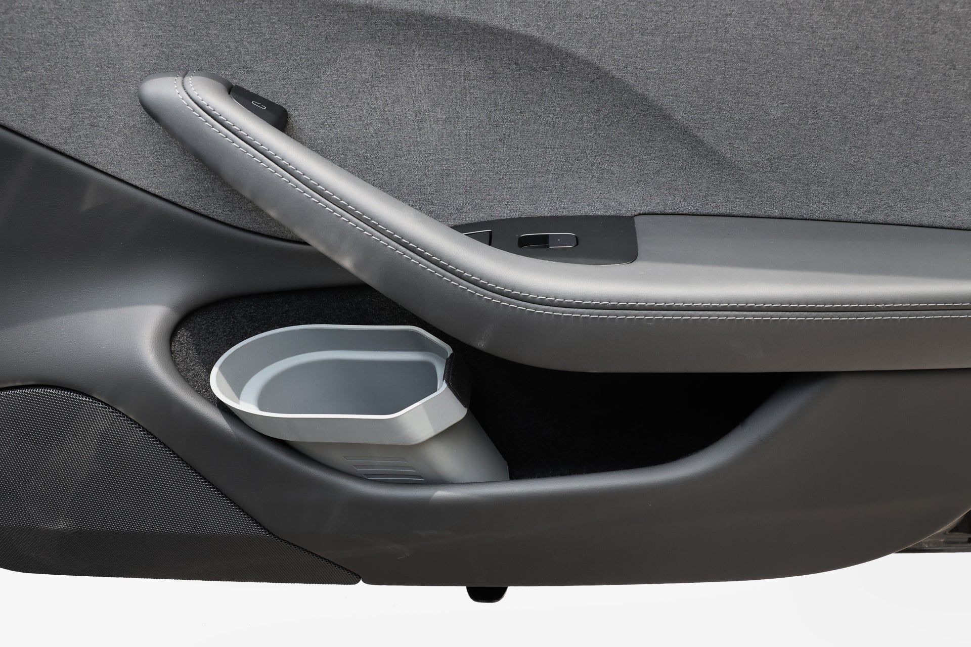 Close-up of a car door interior featuring a gray textured fabric panel, a sleek black armrest with stitching, and a window control panel. The design includes a seamlessly integrated gray silicone storage bin from the JOWUA Door Side Storage Box (Set of 2), offering both style and functionality—a hallmark often associated with Tesla models.