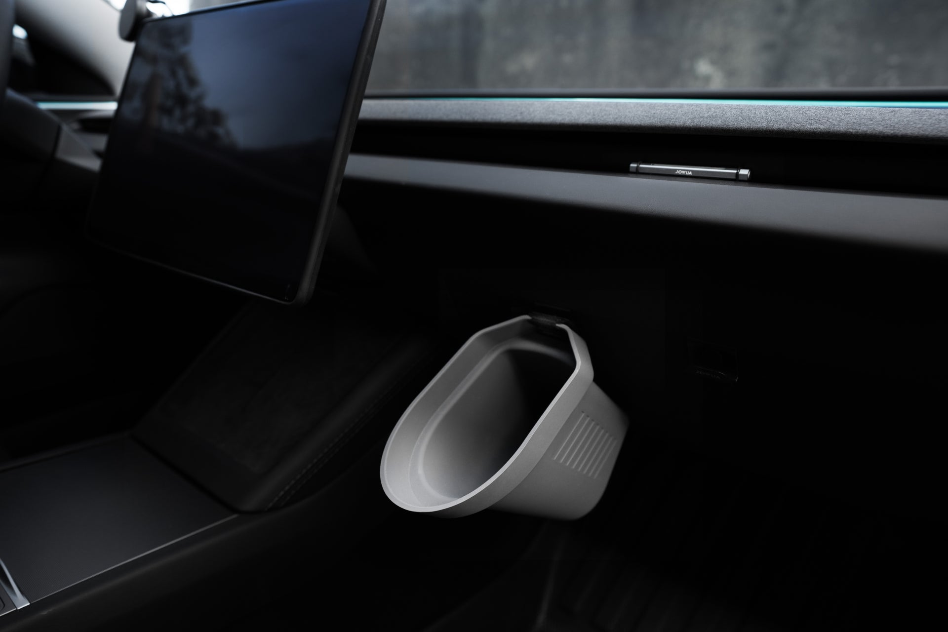 A gray, rectangular JOWUA Door Side Storage Box is attached to the dashboard of a sleek Tesla Model interior, next to a screen. The set of two containers, seemingly made from silicone material, serve as small trash bins that complement the modern design's minimalistic focus.