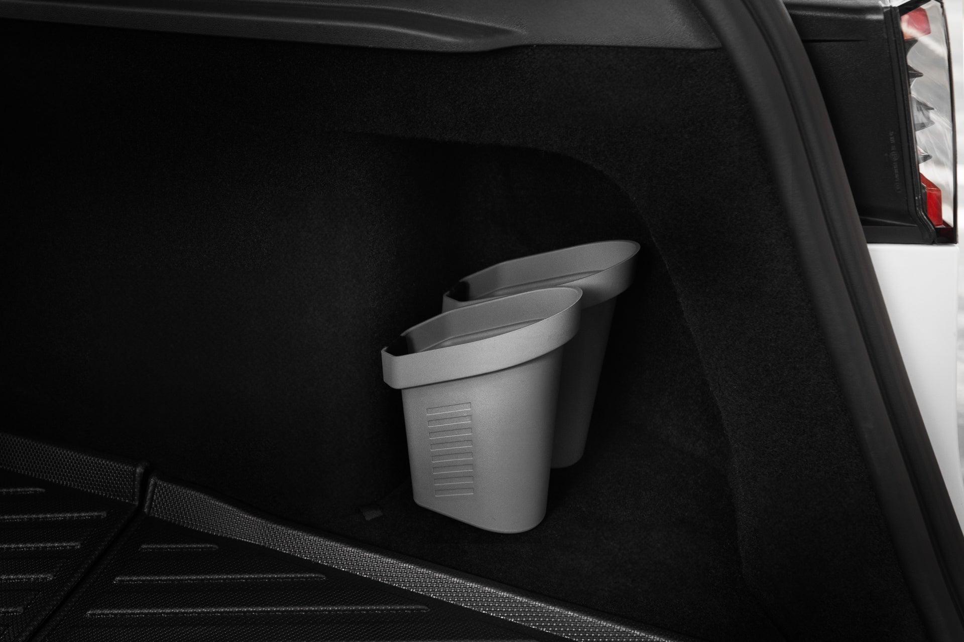 Two small gray Door Side Storage Boxes by JOWUA are neatly positioned against the side wall of a car trunk. The interior is lined with black carpet and features durable silicone material. The sleek white exterior of a Tesla Model is partially visible.