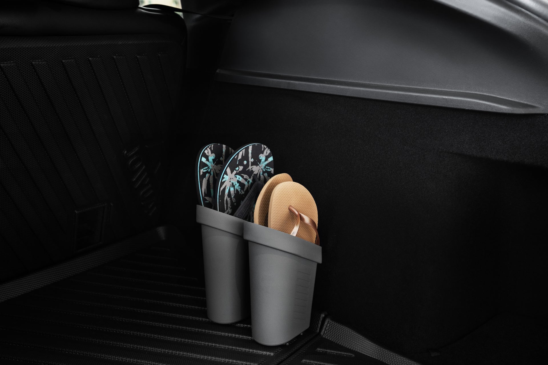 Two pairs of flip-flops, one with a black and white pattern and the other beige, are neatly stored in JOWUA Door Side Storage Boxes (Set of 2) made from silicone material in the corner of a Tesla Model's trunk.