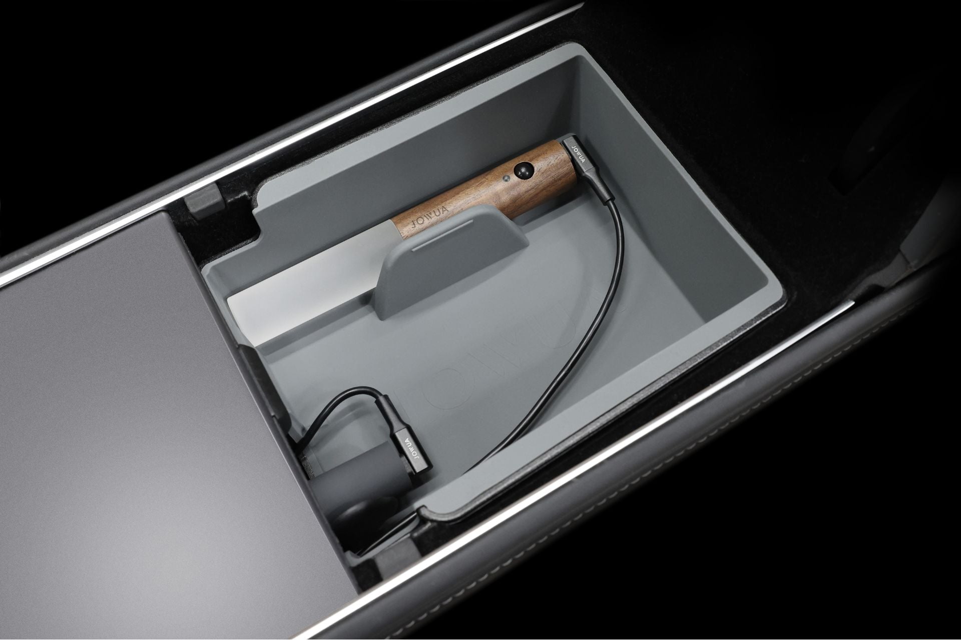 JOWUA's LED Light Bar for the Tesla Center Console illuminates the storage compartment, highlighting a wooden-handled brush and a charging cable neatly arranged against a dark background.