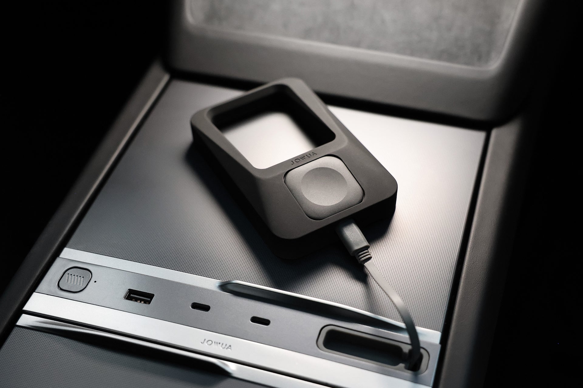 The JOWUA Power Dock Combo, an Apple accessory charger for Tesla, is a black device with a square cutout that connects by cable and rests on the center console near the USB port and control buttons.