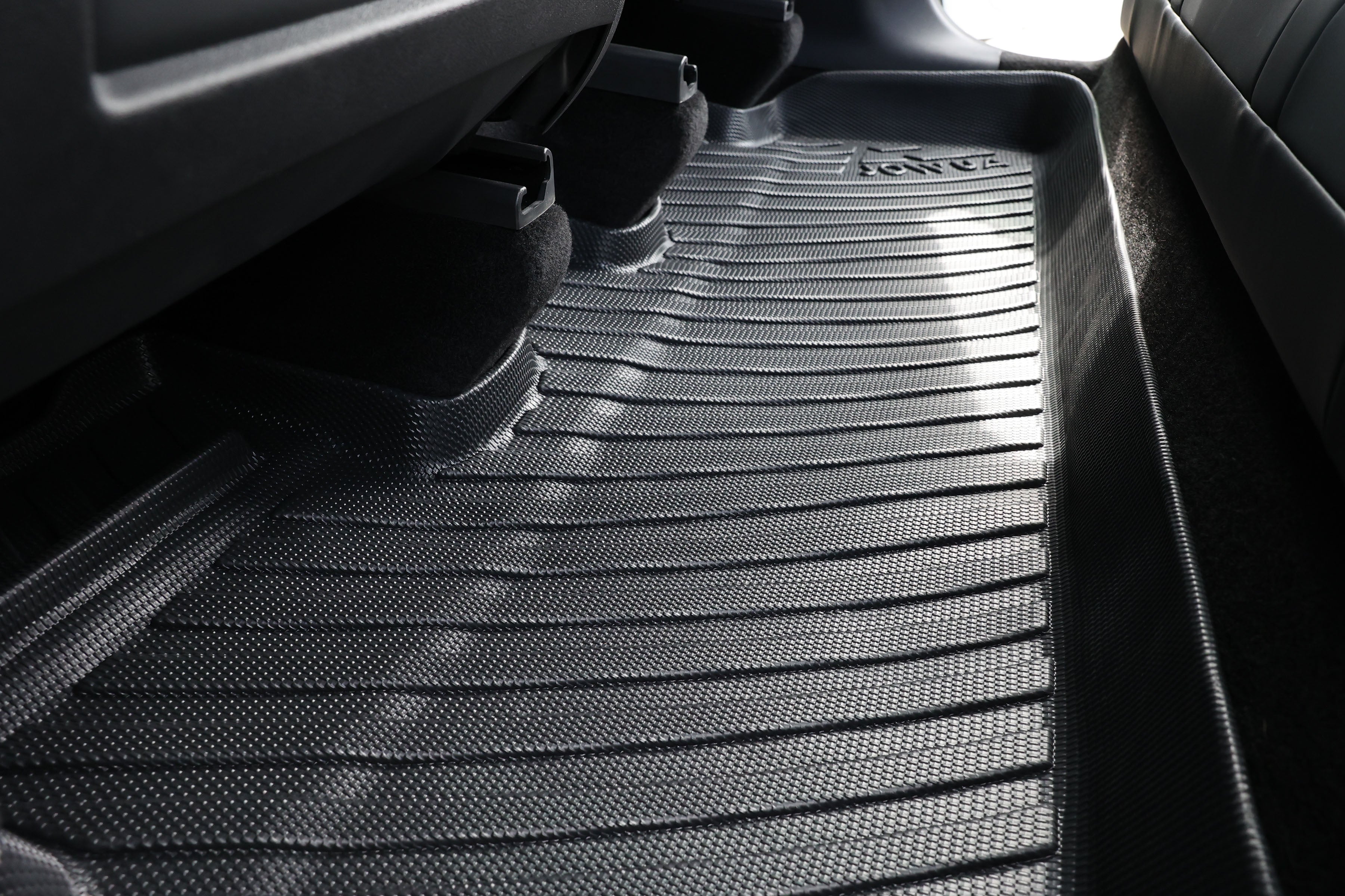 Close-up of JOWUA All-Weather Floor Liners in a vehicle's backseat area. The black mat is grooved and textured with the brand logo visible, fitting snugly to the floor contours—a perfect accessory for Tesla Model Y (Juniper 2025+ / 2021-2024).