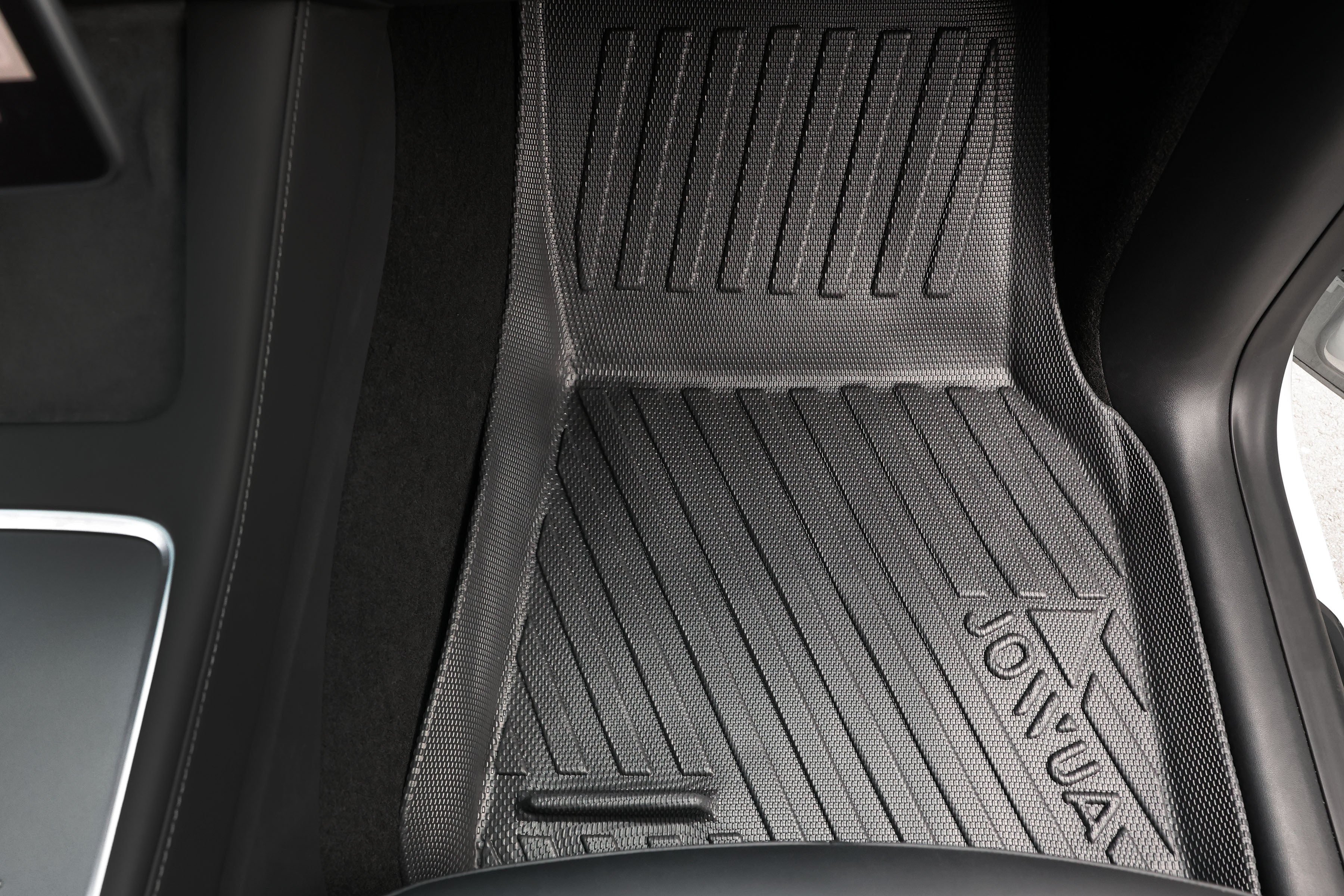 Close-up of an all-weather floor liner with a textured surface and "JOWUA" embossed on it, designed for Tesla Model Y vehicles. The All Model Y All-Weather Floor Liners Combo fits perfectly into the footwell area, complementing the sleek black interior trim.