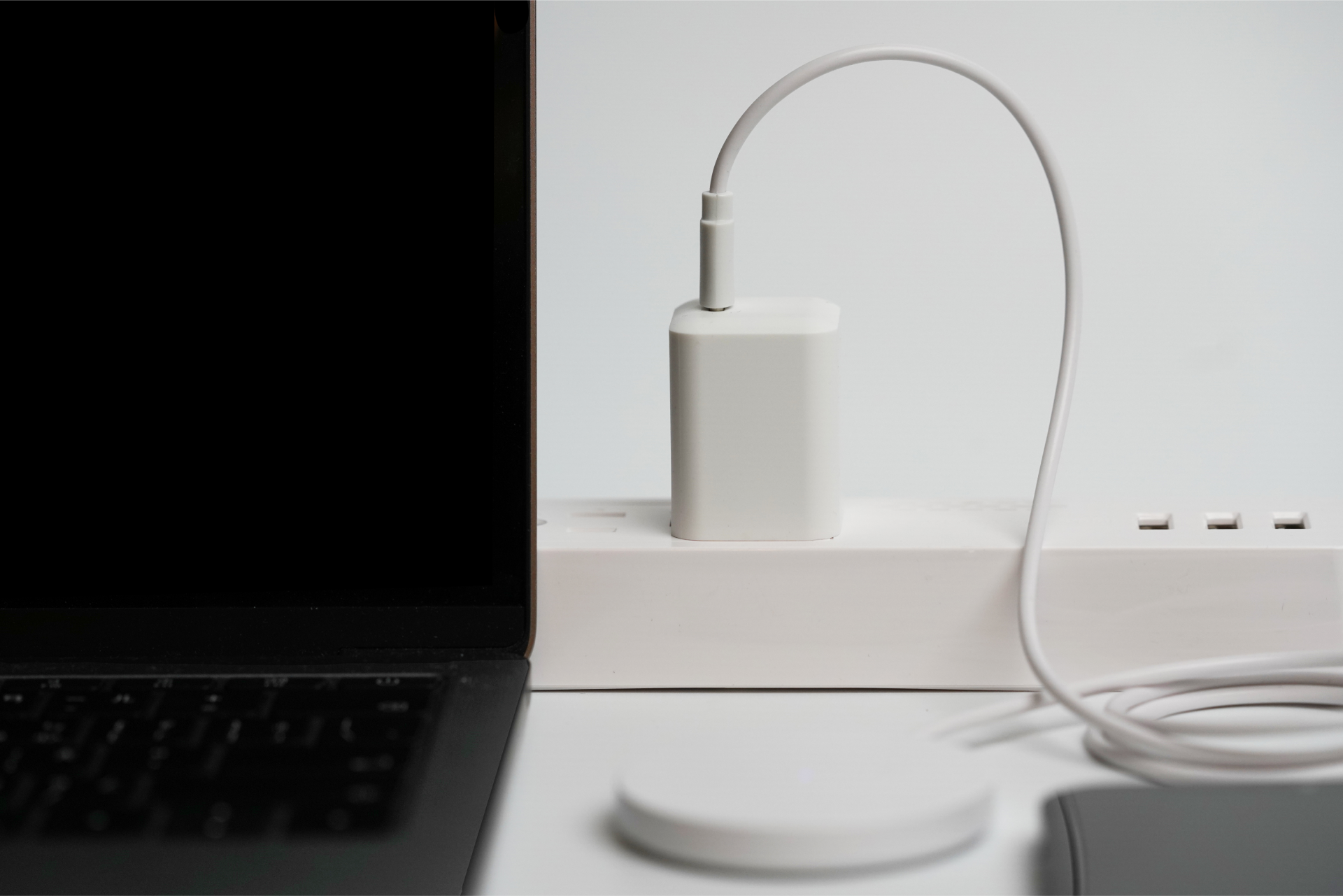 The JOWUA 100W Portable Air Compressor + Charging Solution Kit is plugged into a power strip with a coiled cable for high-speed device charging. A laptop is partially visible on the left, while a wireless charging pad lies in the foreground, ideal for tech enthusiasts.