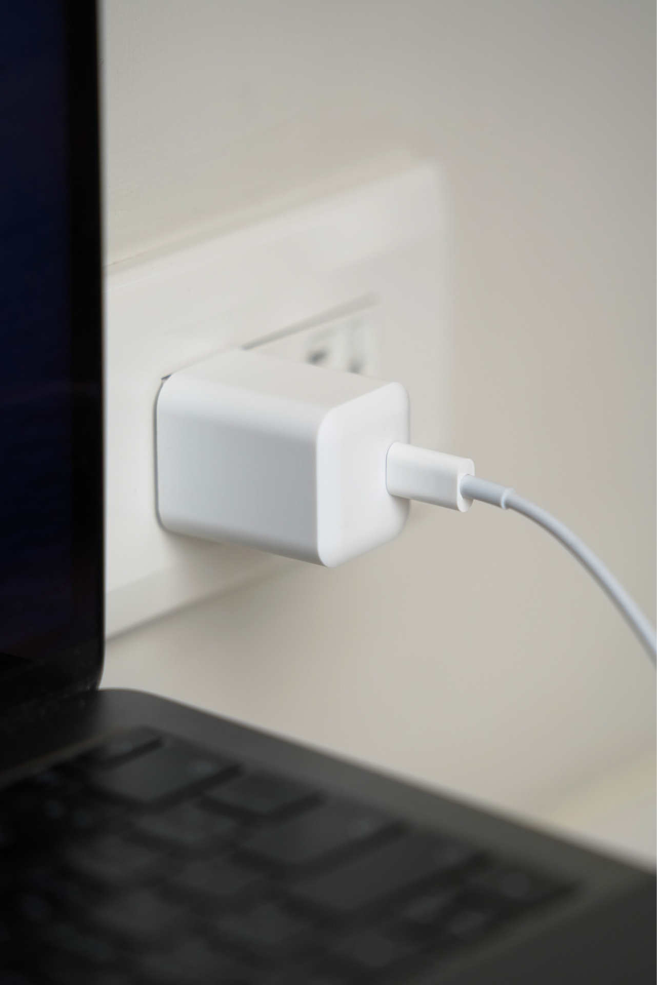 A JOWUA Portable Air Compressor + Charging Solution Kit, featuring a white charger with 60W high-speed charging capability, is plugged into a wall socket, with a cable connected to a laptop positioned on a nearby surface.