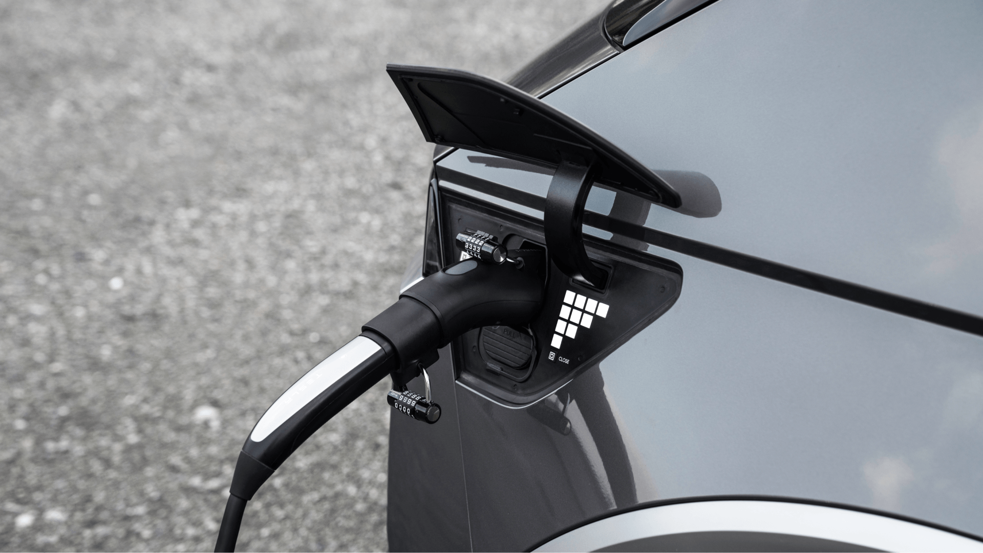 A close-up image features an electric vehicle being charged using the JOWUA TPC(NACS) to J1772 Adapter. The sturdy charging cable is connected to the car's AC charging port, with the flap open. The silver vehicle is parked on a rough, gray surface.