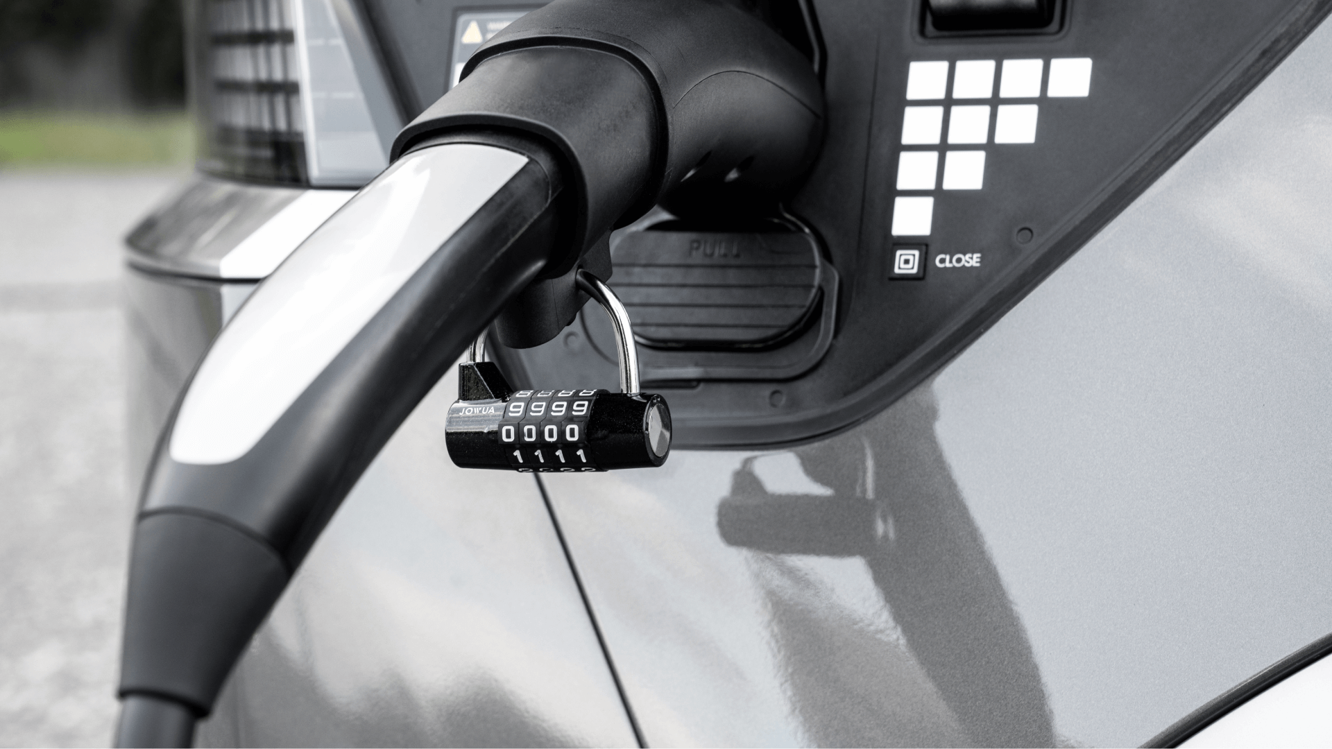 A close-up displays the charging port of an electric car with a JOWUA TPC(NACS) to J1772 Adapter securely inserted. The adapter features a silver combination lock to enhance its durability and ensure security, while the car's shiny surface reflects light elegantly against a blurred background.